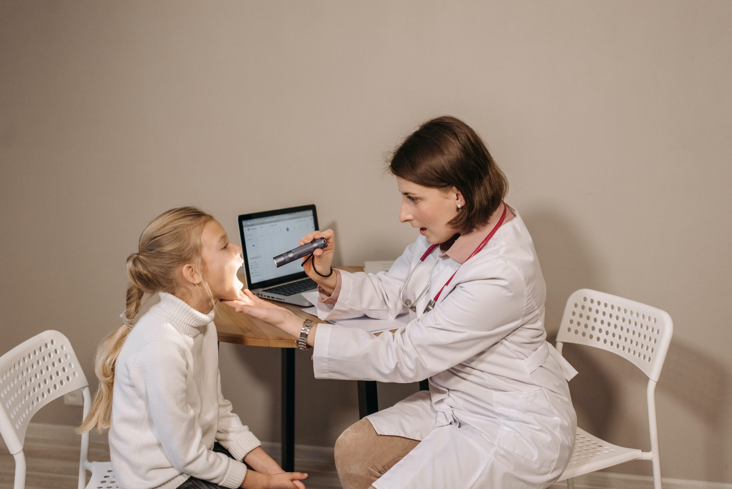 Lekarka pediatrka, zaglądająca do gardła małej dziewczynce w swoim gabinecie