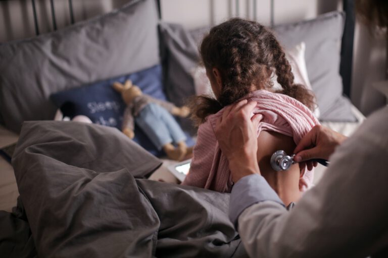 Lekarz pediatra osłuchujący małą dziewczynkę w łóżku
